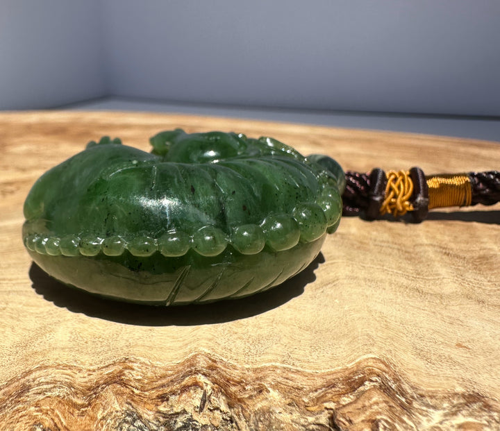 Close up of the carved green jade pendant Qi Lin with a portion of braided cord visible on a wooden surface
