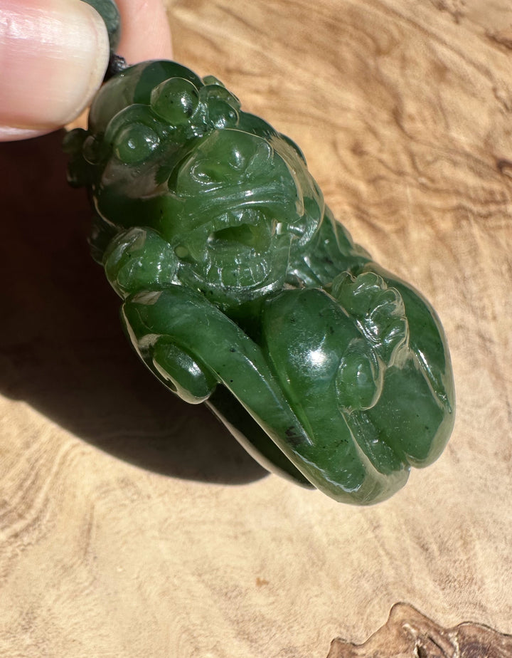 Close-up of a carved green jade Qi Lin pocket pendant being held by a finger on a dark cord.