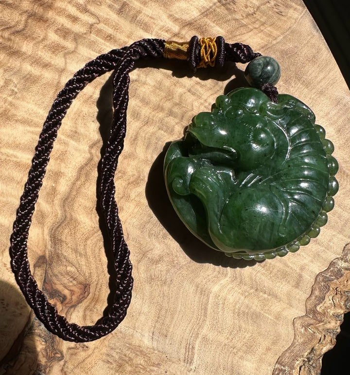 Dark braided necklace with gold wrap coils near the top and a green jade Qi Lin pendant resting on a tan fabric background.