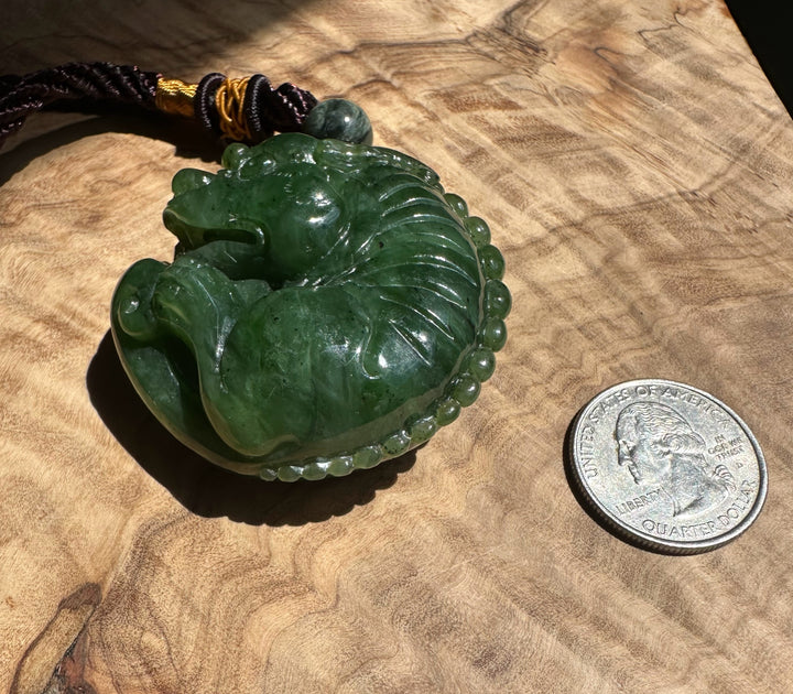 Green jade Qi Lin pocket pendant with bead accents shown with coins for scale on a textured surface.