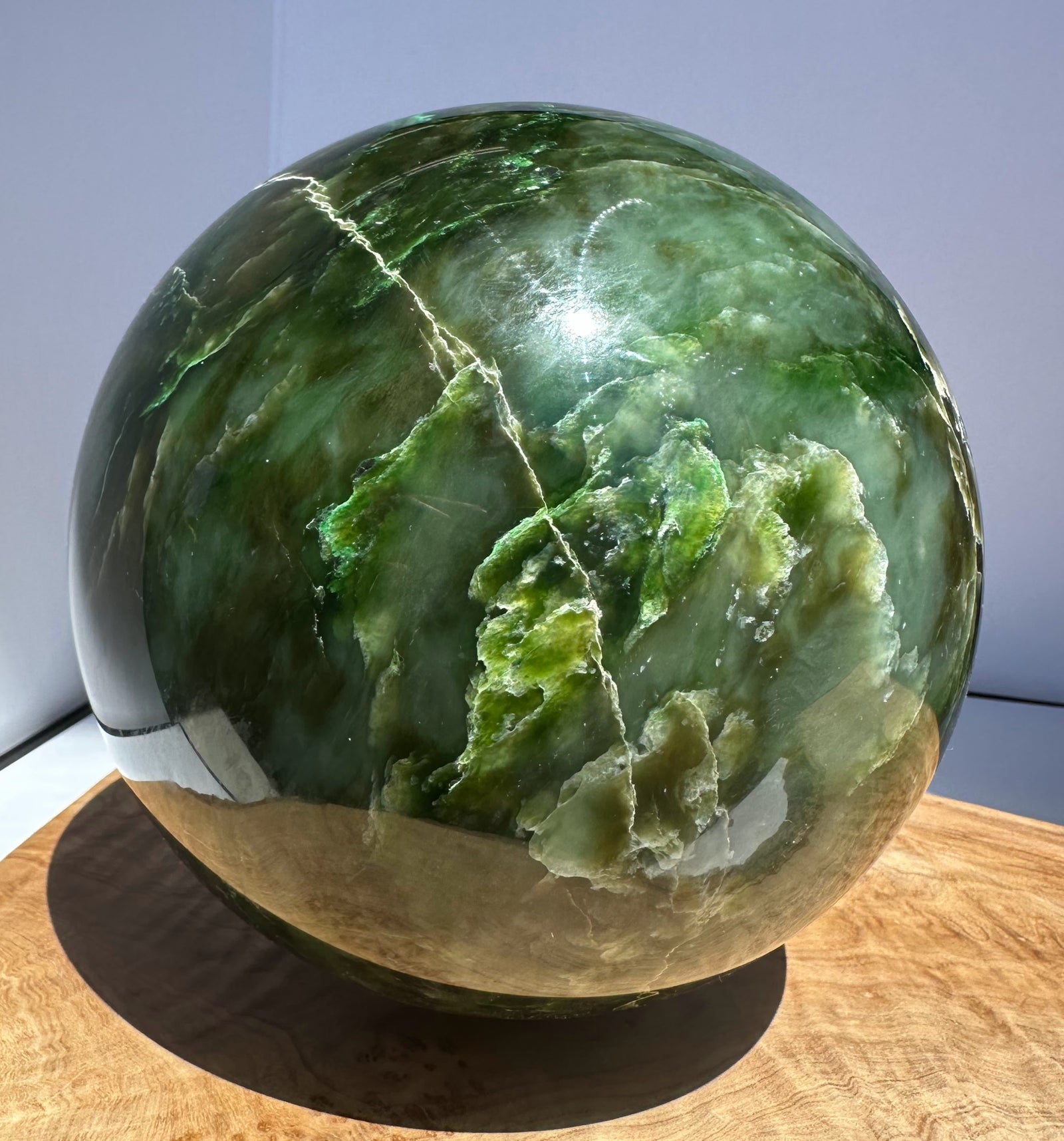 6 inch Polar Jade Sphere weighing 15.4 lbs with deep green hues and white veining resting on a wooden base