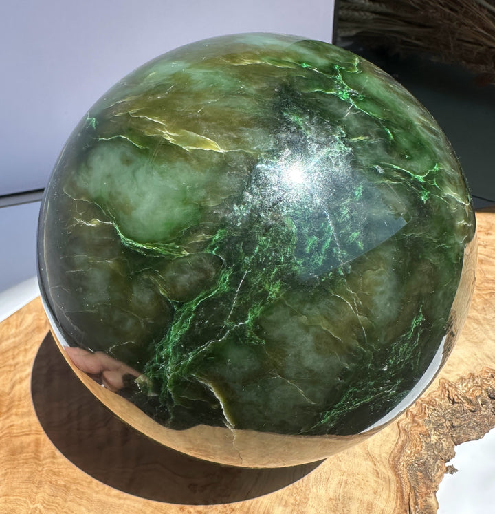 Hand holds a 6 inch Polar Jade Sphere showing vivid green color and white veining on a wooden base