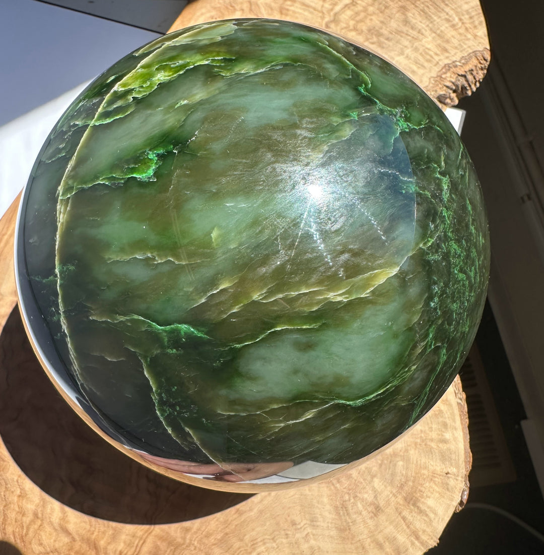 Close-up of a 6 inch Polar Jade Sphere showing deep green with lighter veins on a wood display base