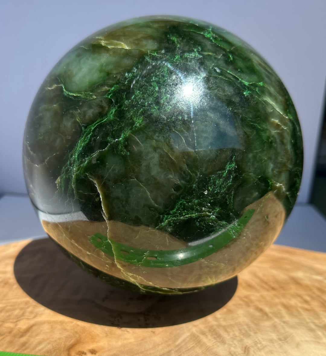 Side view of a 6 inch Polar Jade Sphere with vivid green banding against a light background