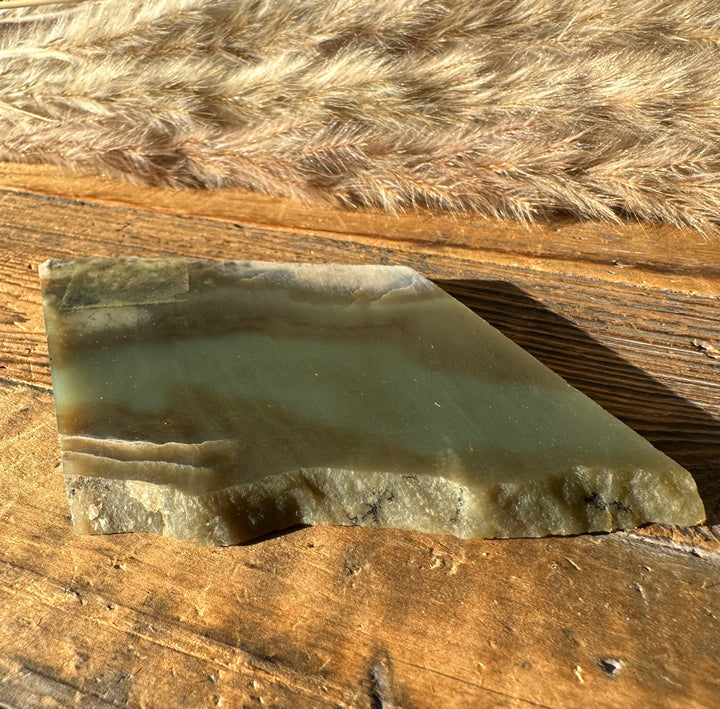 Wyoming Nephrite Slab 80g green gray surface with natural serrated edge on wood backdrop