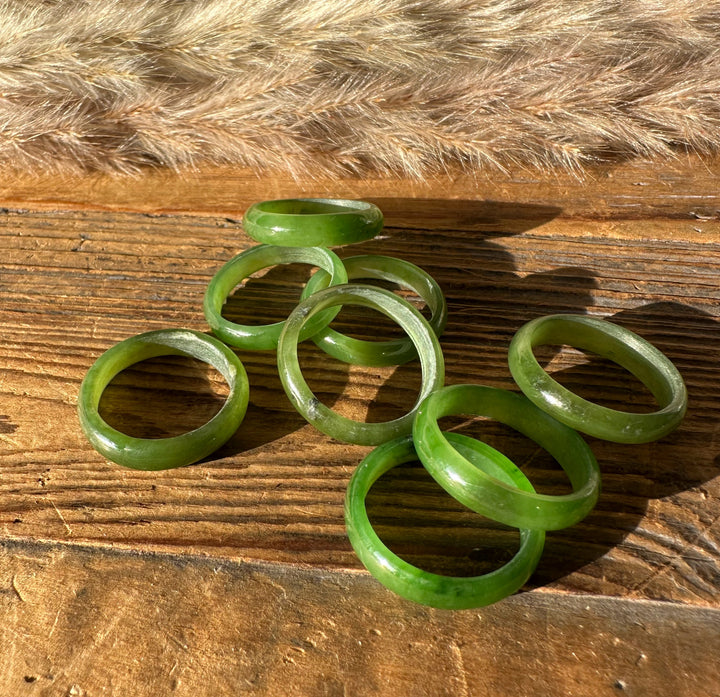 Jade green band rings in several widths laid on a weathered wooden surface
