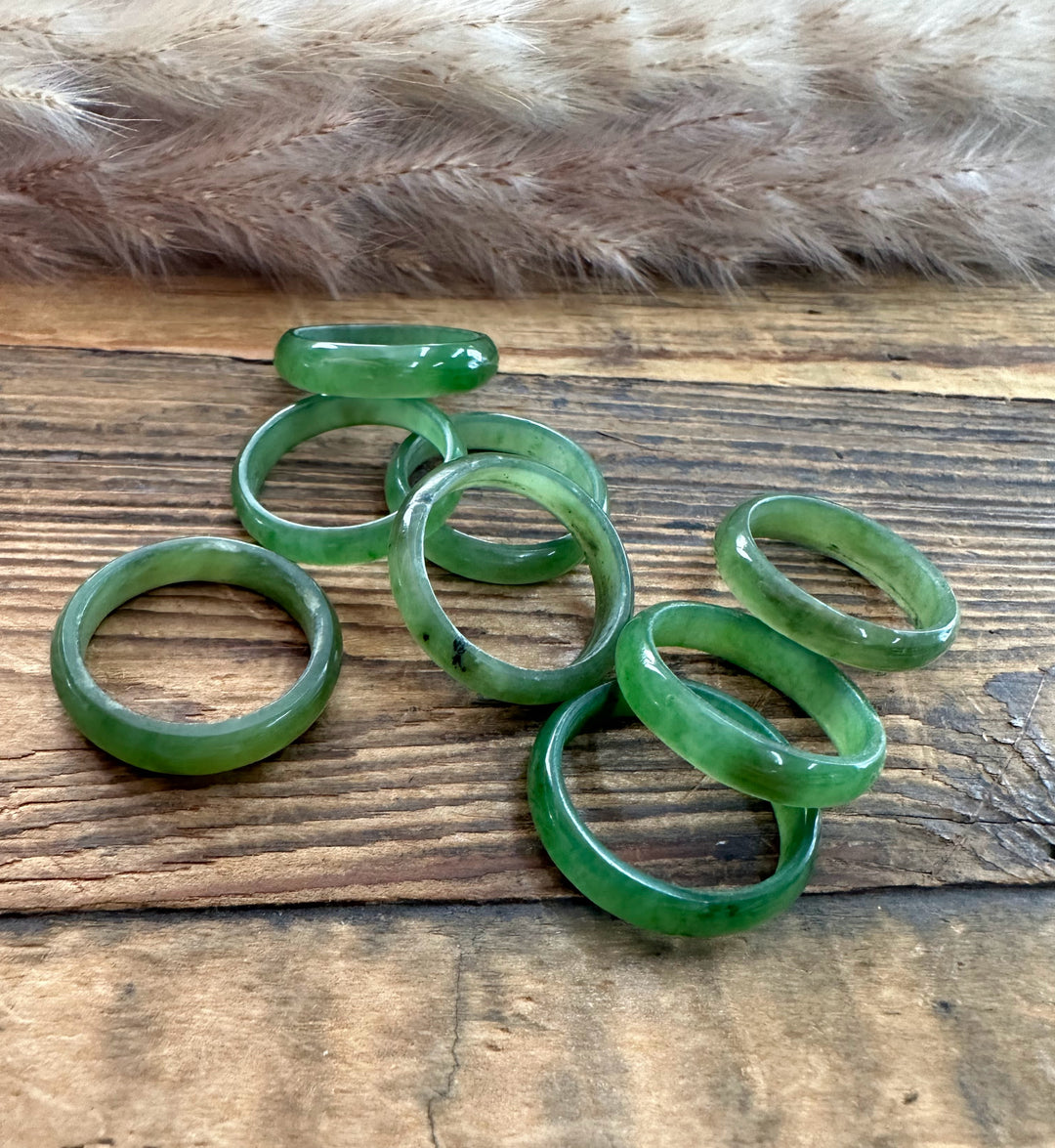 Group of green jade band rings in varying widths arranged on a rustic wooden surface