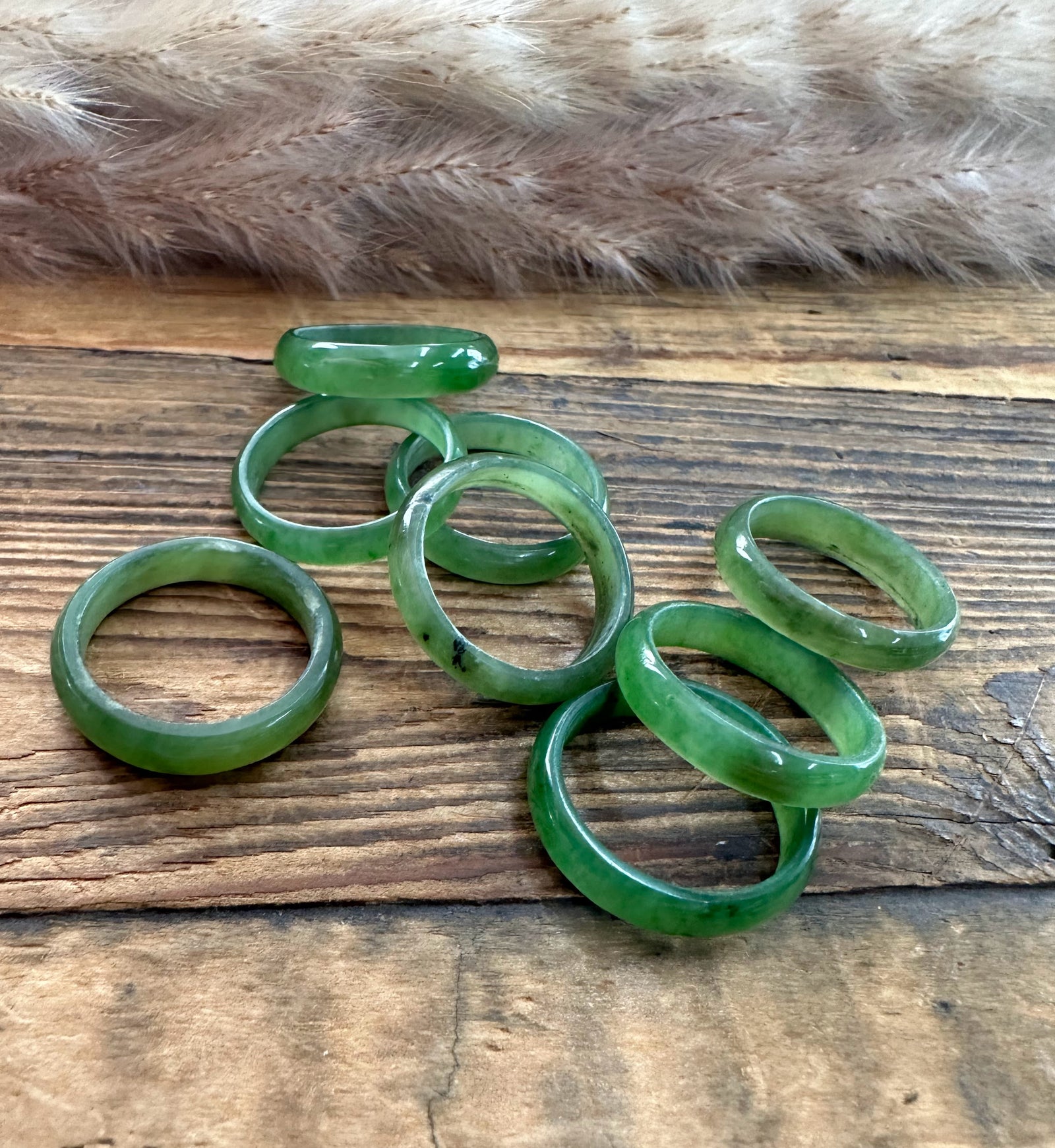 Group of green jade band rings in varying widths arranged on a rustic wooden surface