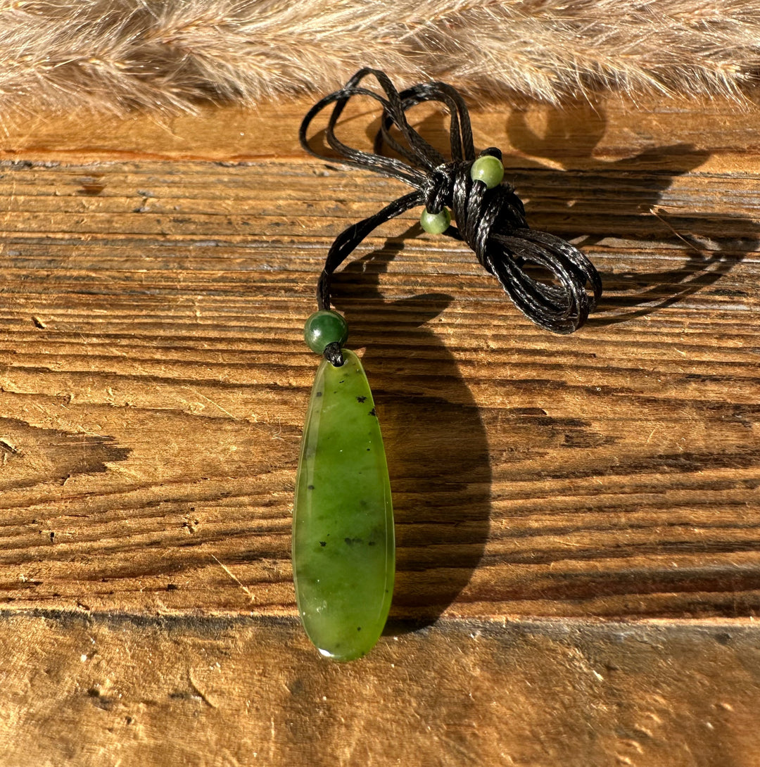Canadian Jade Teardrop Pendant on black cord with green beads resting on a wood surface
