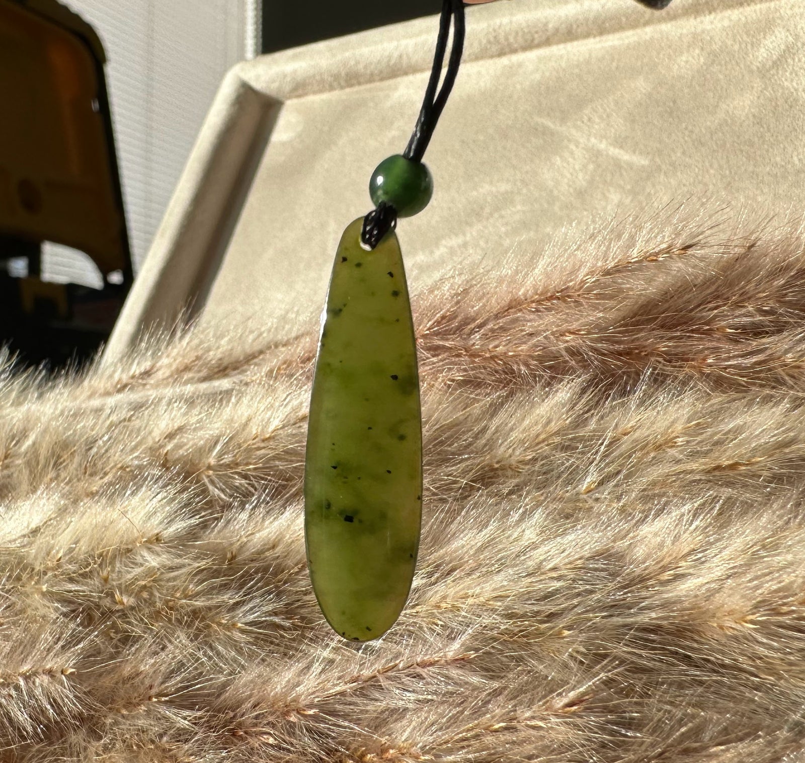 Canadian Jade Teardrop Pendant on black cord with green bead against a beige faux fur backdrop