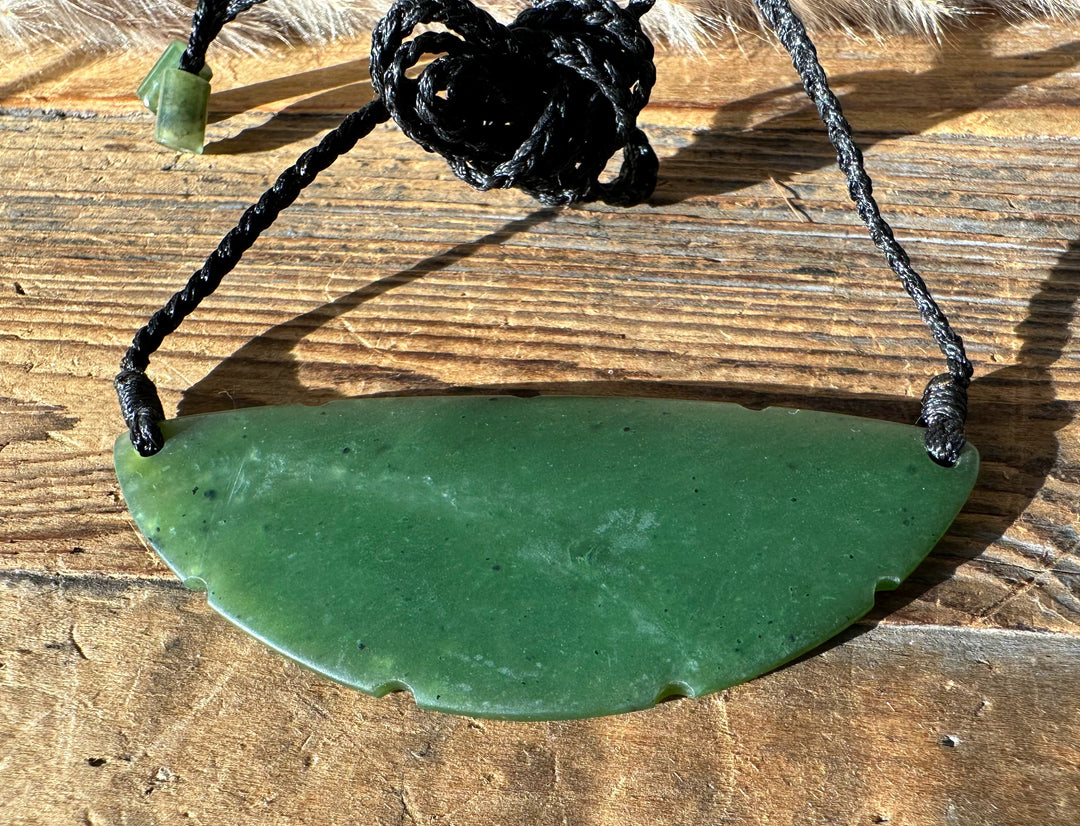 Green jade crescent pendant on braided black cord with a pale green bead near the top and a bead on the end