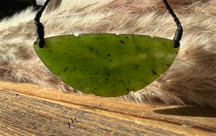 Canadian Jade Pendant 1979 green jade crescent with two holes for a cord on a wood and fur backdrop