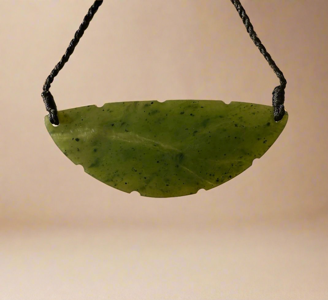 Curved green jade pendant with irregular bottom notches suspended on a black cord