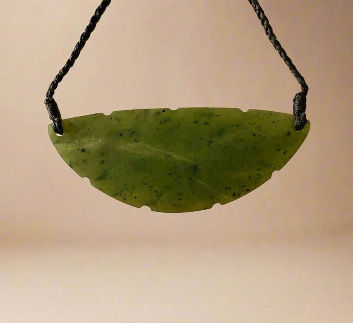 Curved green jade pendant with irregular bottom notches suspended on a black cord