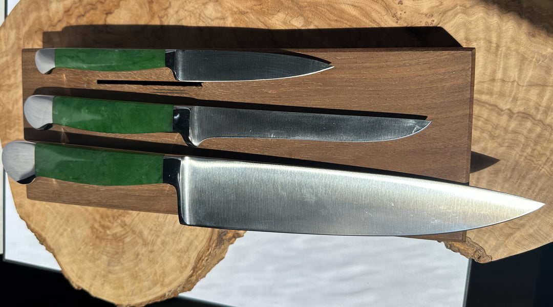 Set of three knives with green handles in a wooden holder on a wooden surface