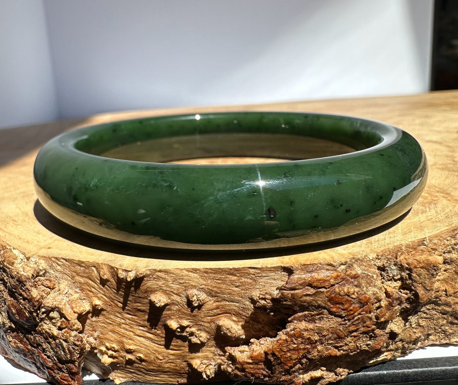Dark green Canadian jade bangle with a smooth polished finish resting on a wooden surface
