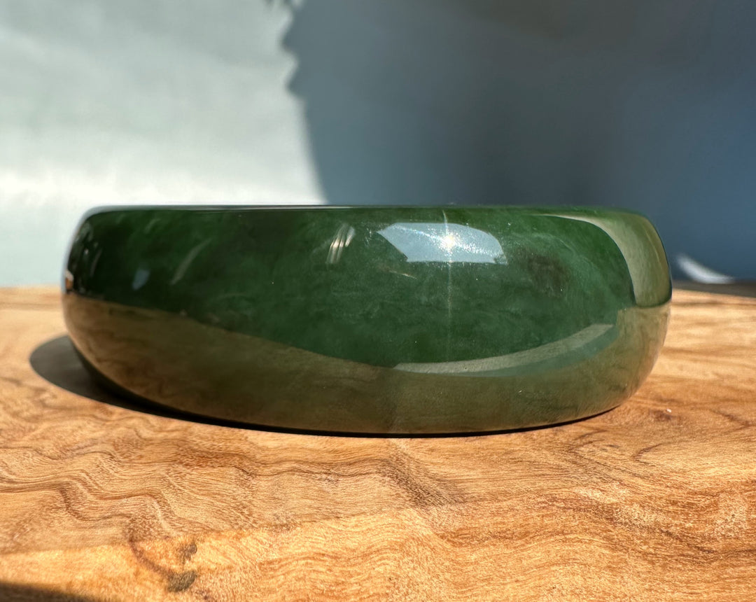 Deep green jade bangle 61 x 22mm with a polished finish resting on a wooden surface