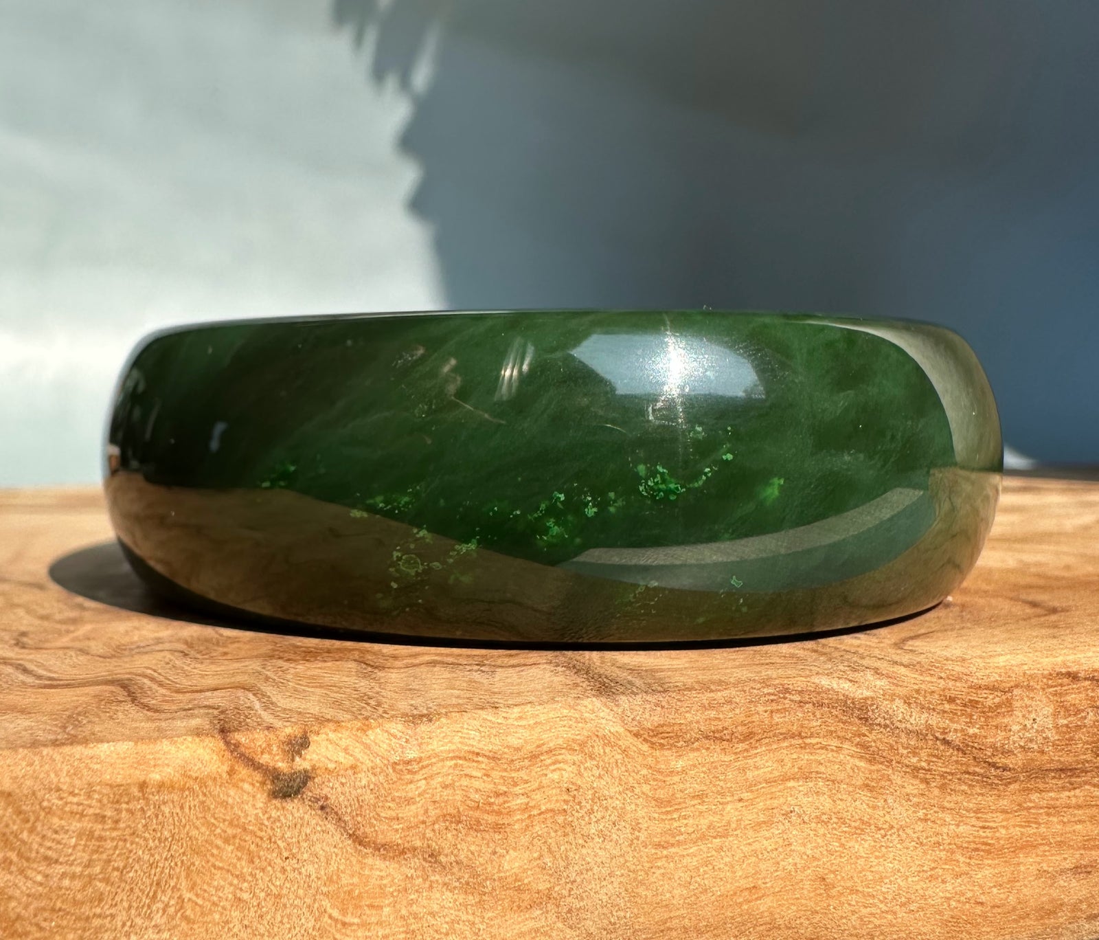 Polished dark green jade bangle sized 61 by 22 mm resting on a wooden surface