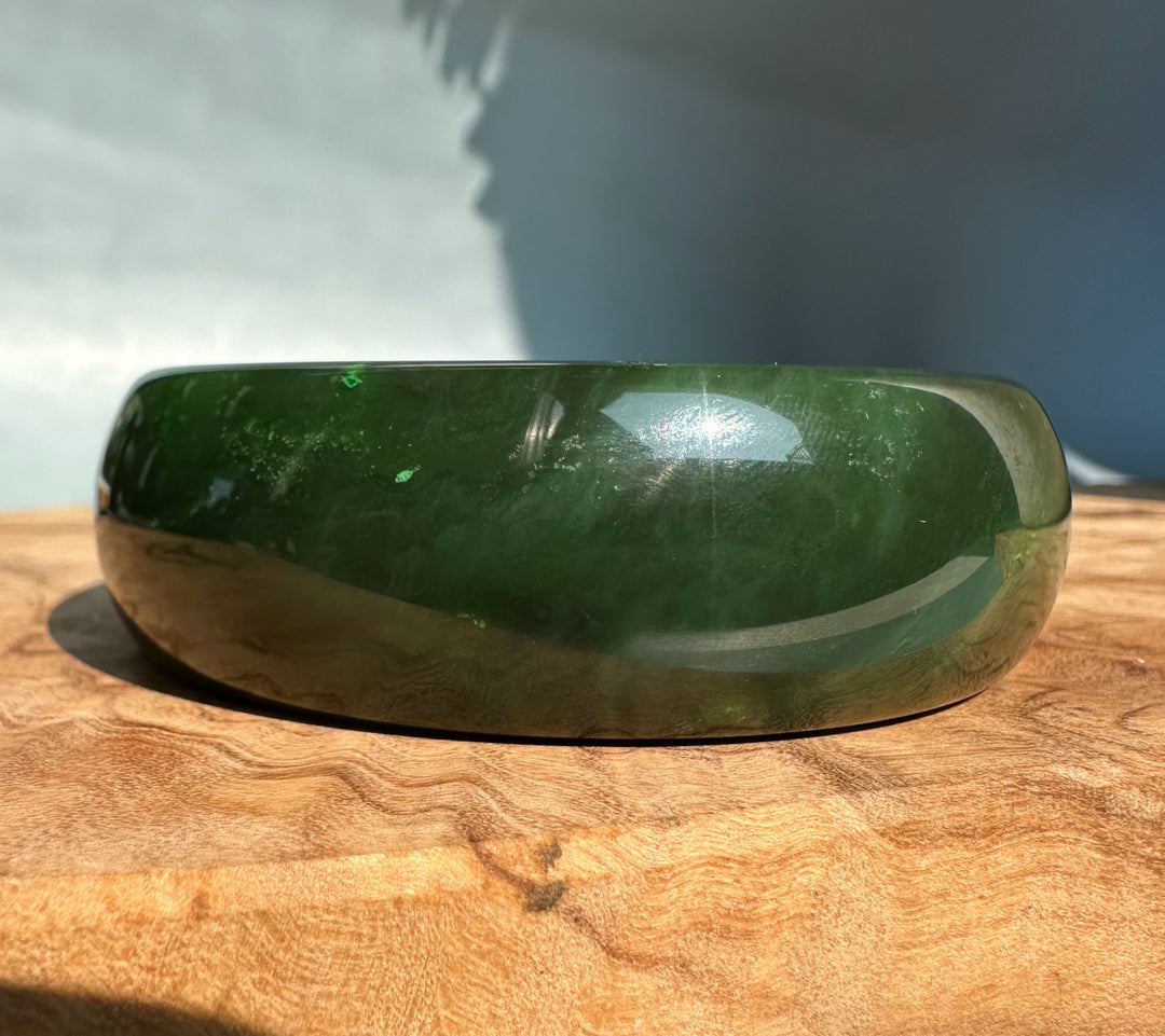 Glossy dark green jade bangle 61 x 22 mm resting on a wooden surface