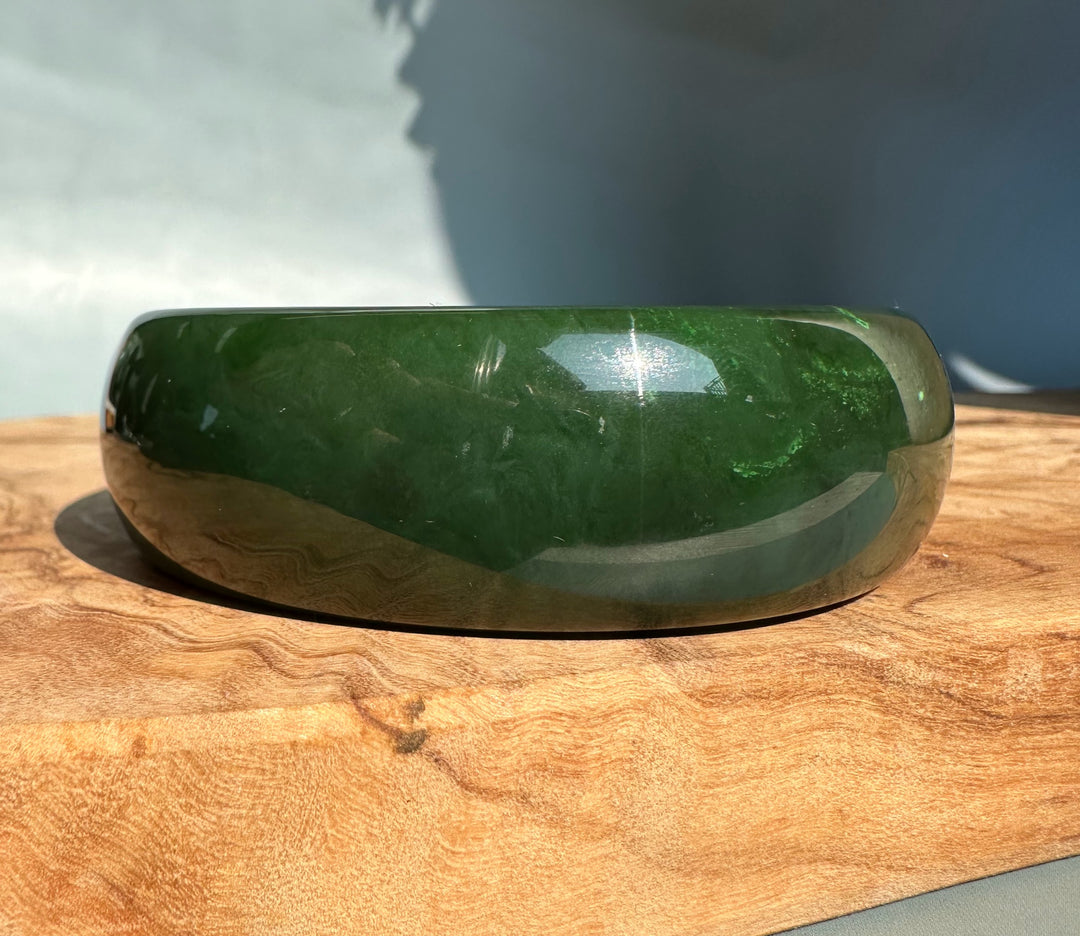 Side view of a smooth green jade bangle on a wooden surface with polished sheen