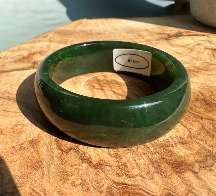 Green jade bangle resting on a sunlit wooden surface with a size tag inside