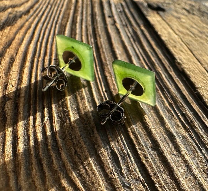 Green jade square pyramid stud earrings with silver posts on a weathered wooden surface.