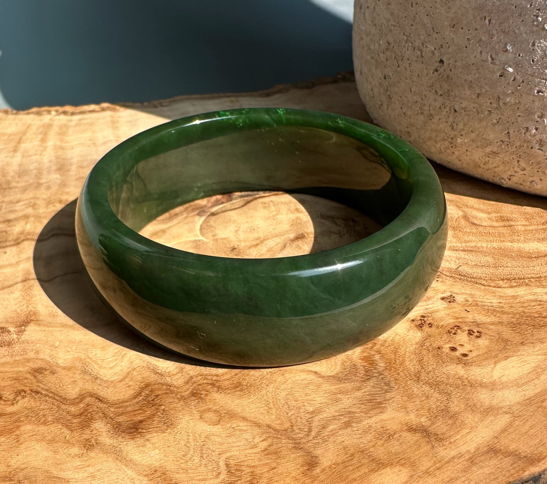 Green jade bangle 61 x 22 mm with a glossy finish on a wooden surface