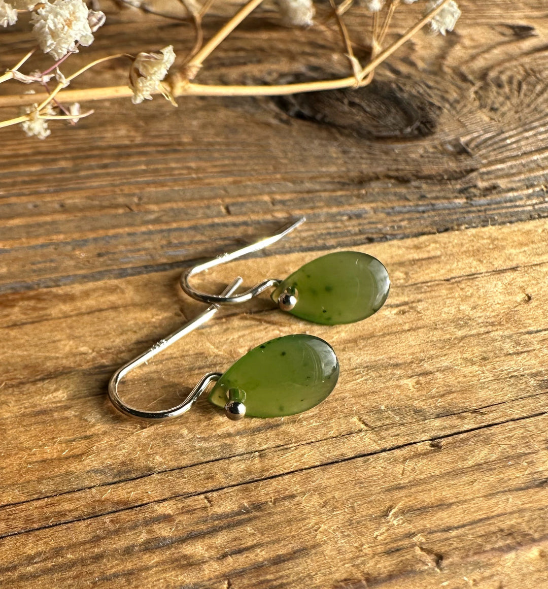 Close up of jade teardrop earrings with silver hooks on a wood surface