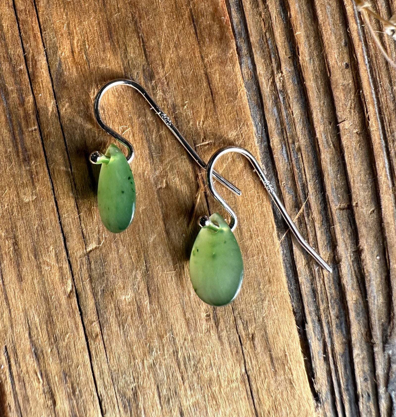 Green jade teardrop earrings with silver hooks on a rustic wooden surface