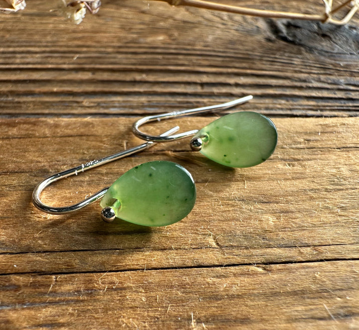 Close-up of jade teardrop earrings with silver hooks resting on a wooden surface