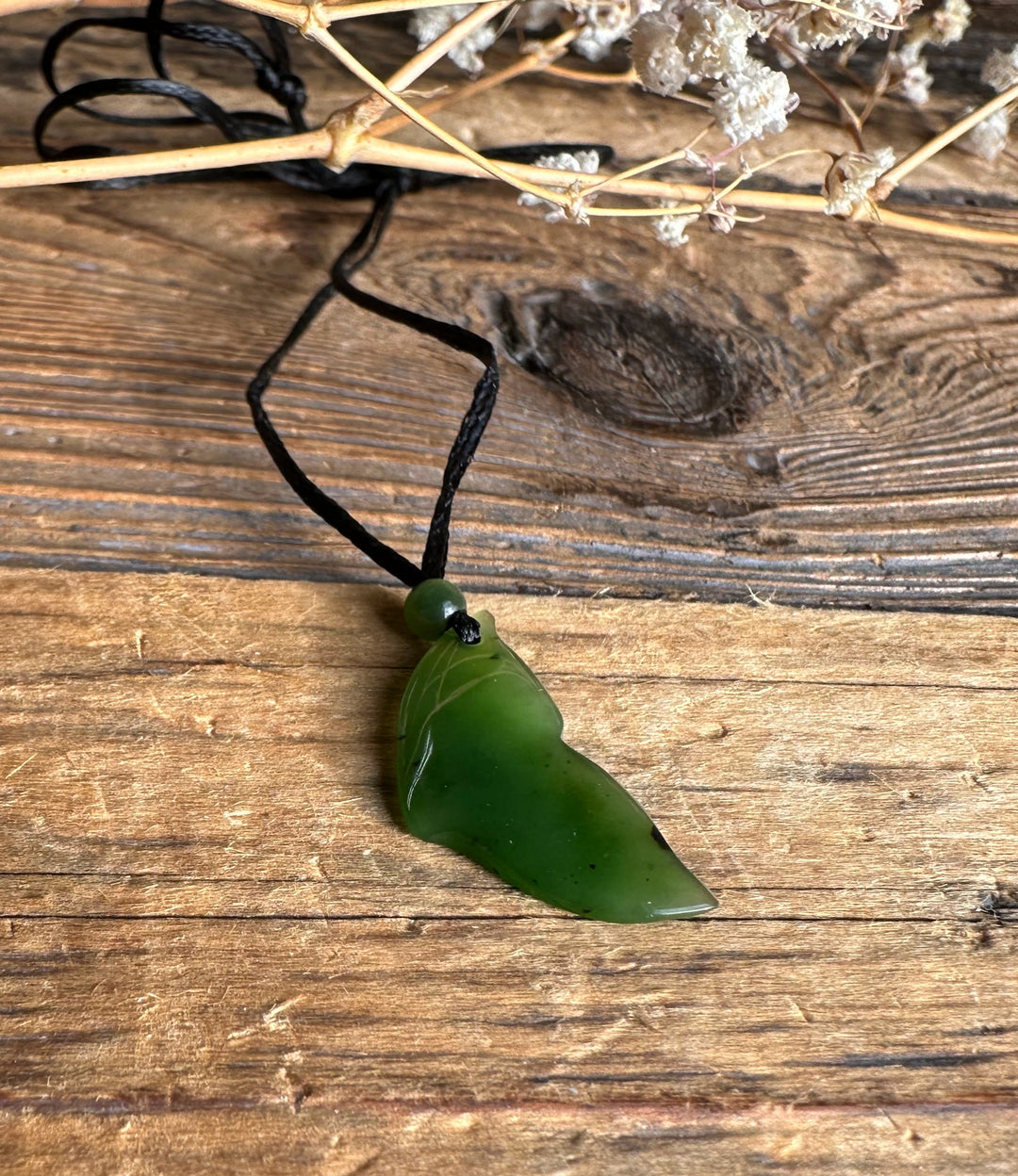 23mm green jade whale tail pendant on a black cord against a rustic wooden surface