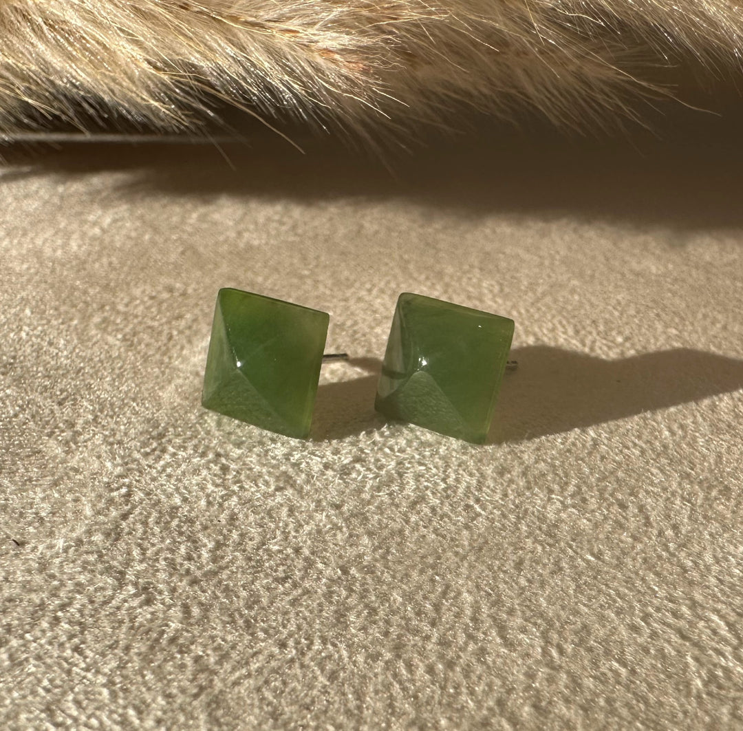 Green jade square pyramid earrings 15mm placed on sandy surface with a tuft of fur above.