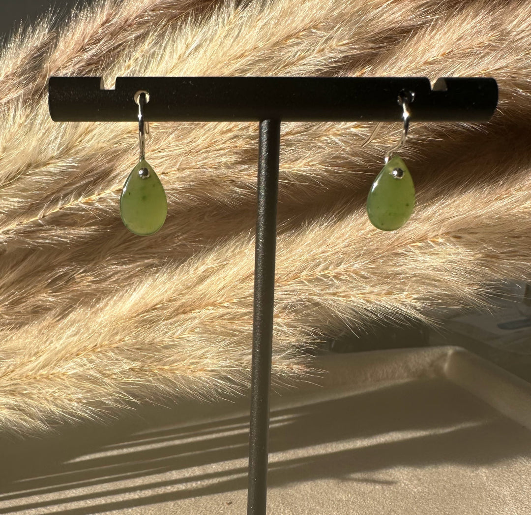 Jade teardrop earrings with silver hooks hanging from a black display bar against a beige fur backdrop