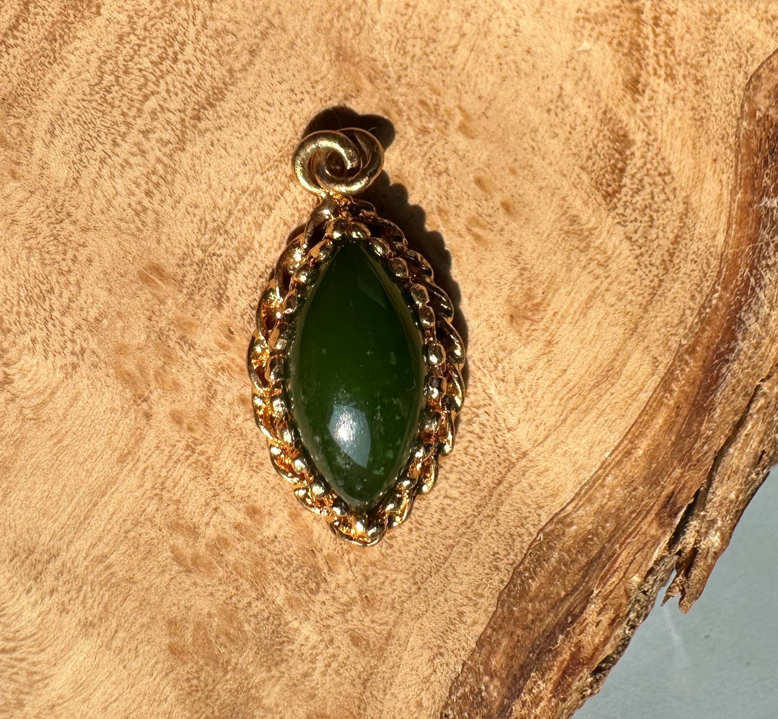 Jade marquise pendant with twisted gold border on a wood background