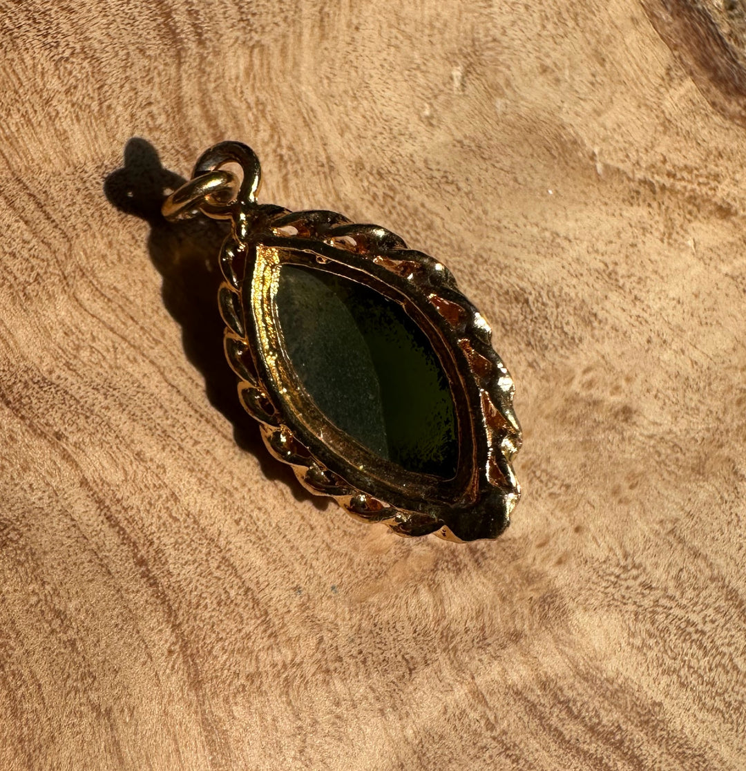 Dark green jade marquise pendant with a gold scalloped frame resting on a rustic wooden surface.