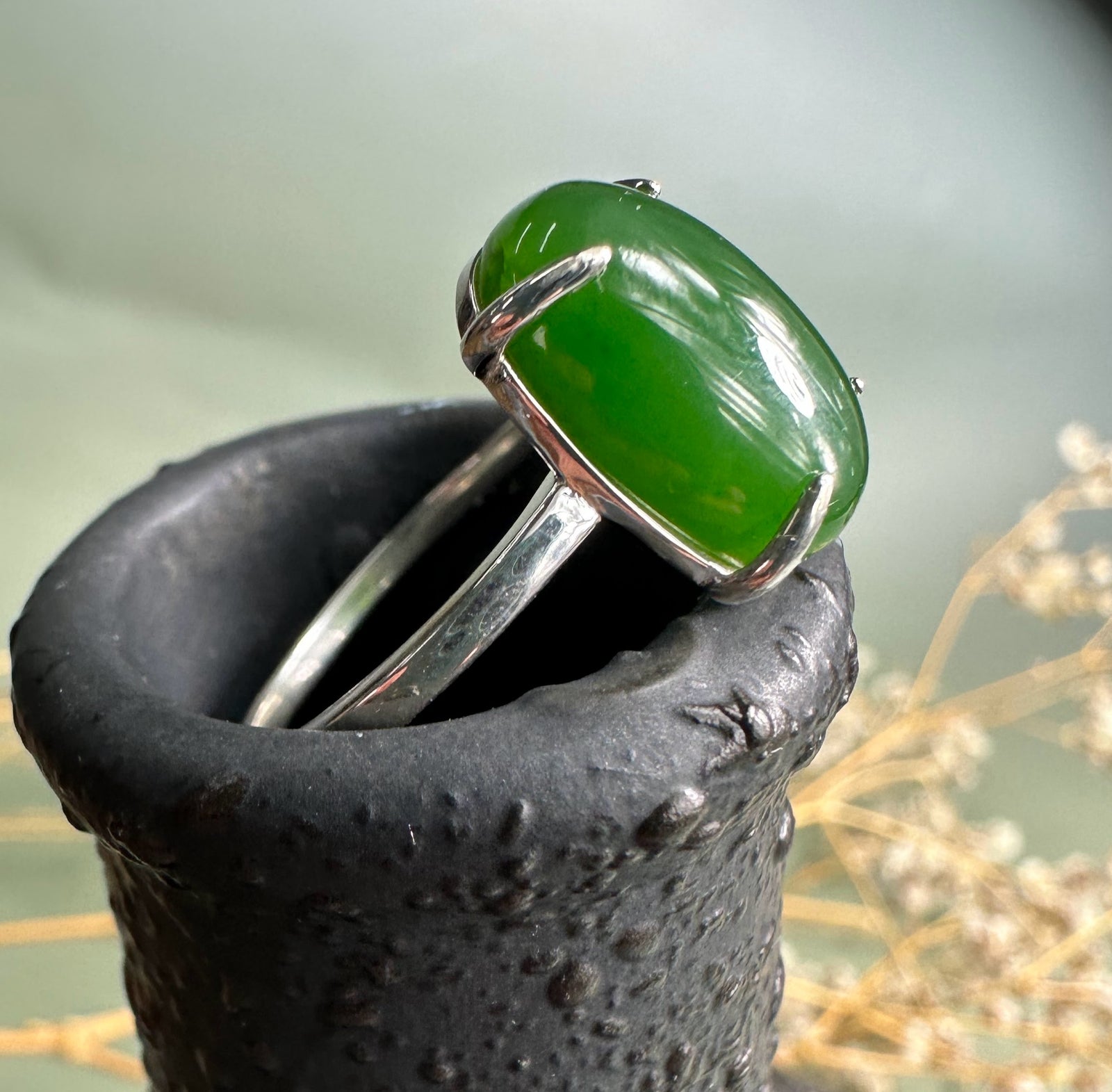 Close-up of the Canadian jade and silver ring on a textured black stand highlighting the green oval jade stone