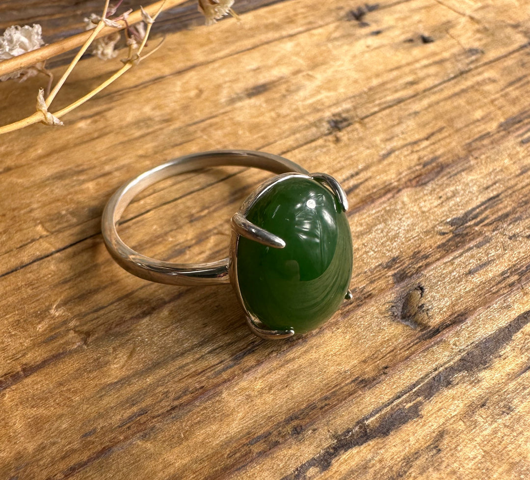 Canadian Jade and Silver Ring sits on a wooden surface with a green jade cabochon secured by a silver prong setting.