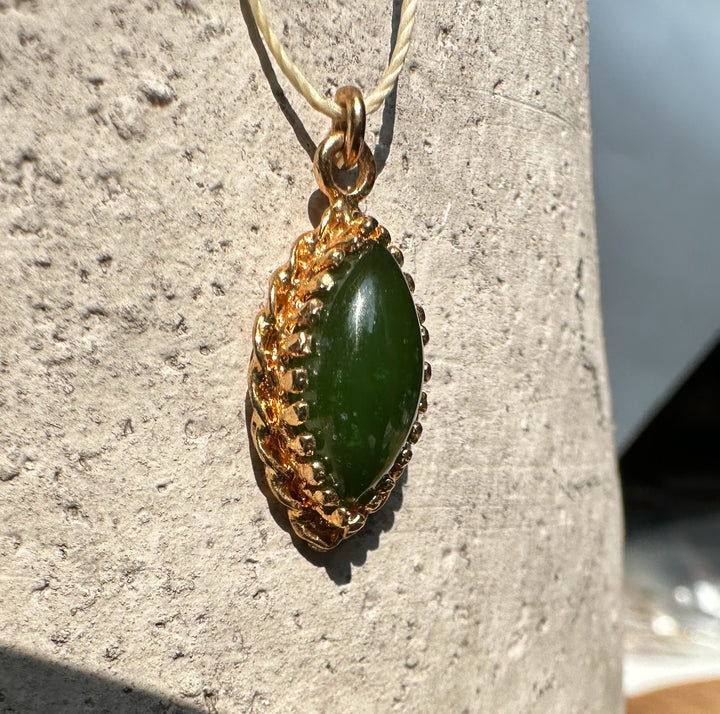 Green jade marquise pendant in an ornate gold bezel on a light cord.