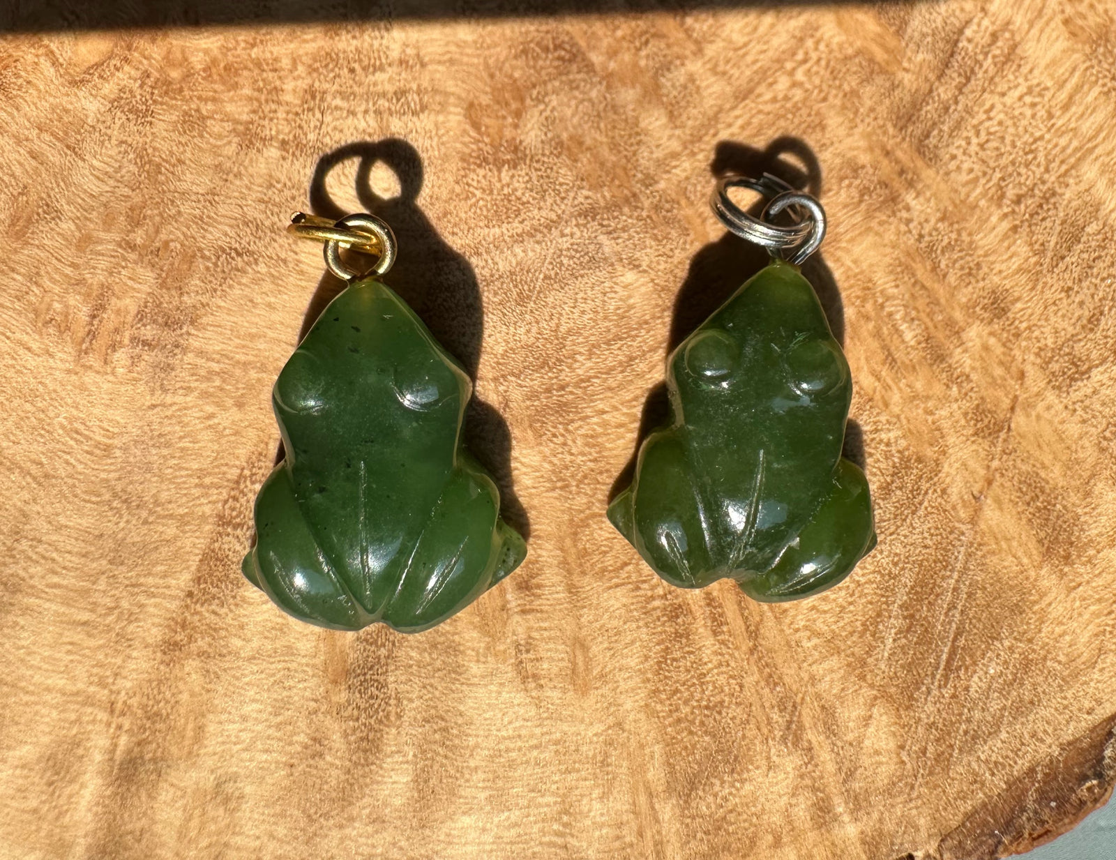 Two flat green frog charms with gold and silver loops on a wooden background