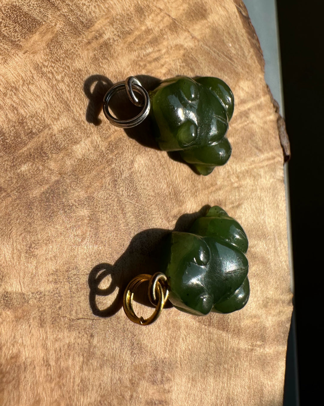 Two green jade frog charms with silver and gold hoops on a wooden surface.
