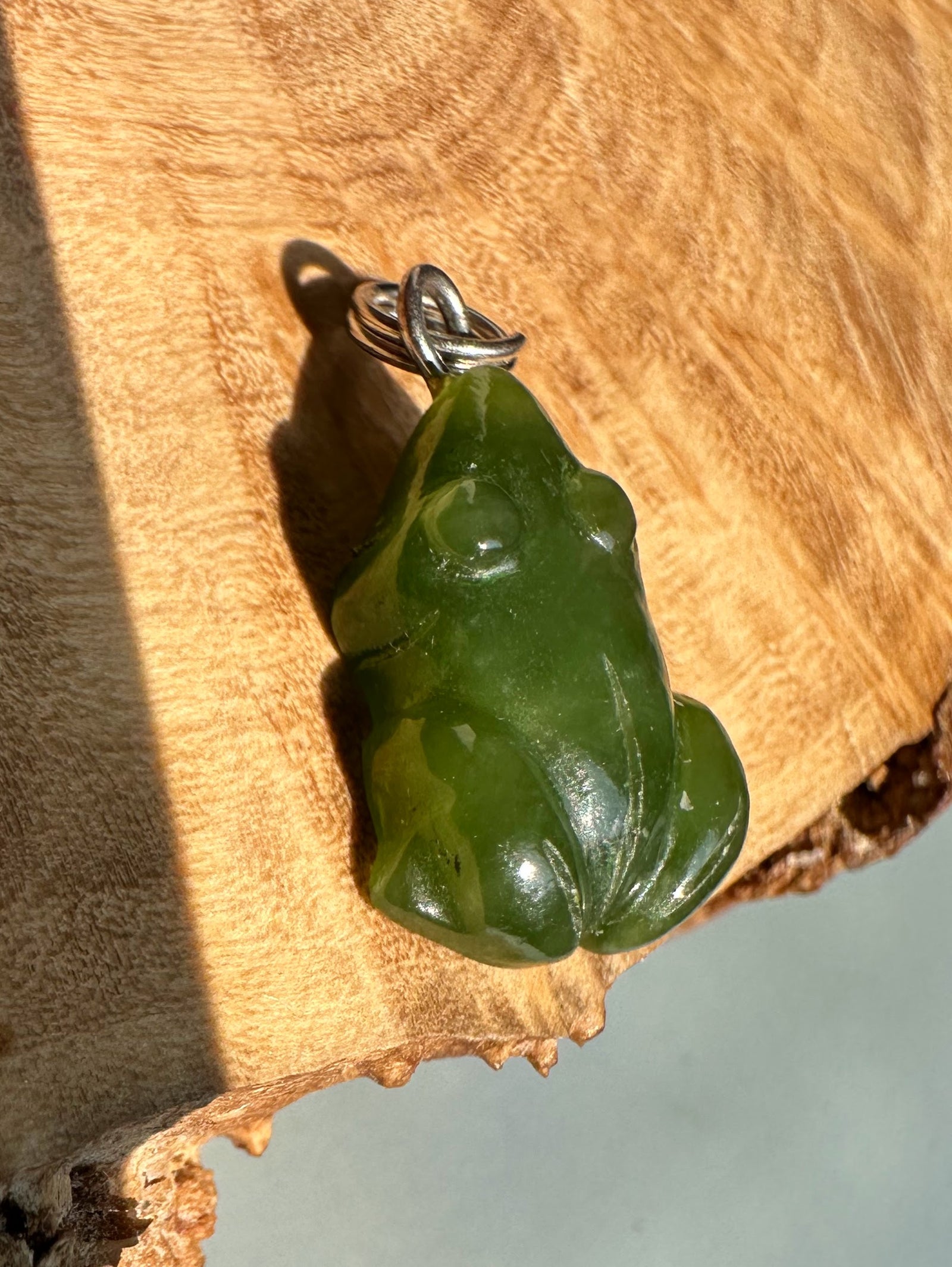Green jade frog charm with a metal bail on a wooden surface.