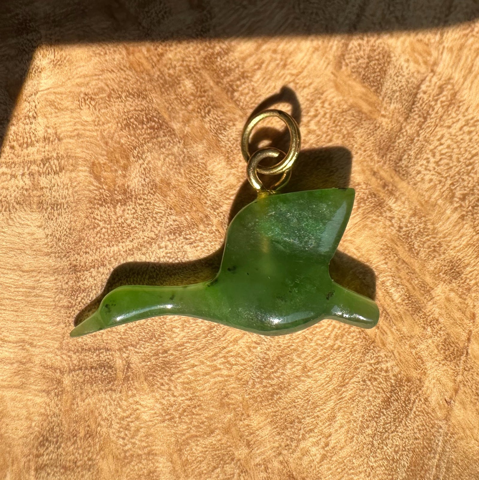 Canadian Jade Goose Charm 23mm with a gold ring bail on a textured brown surface