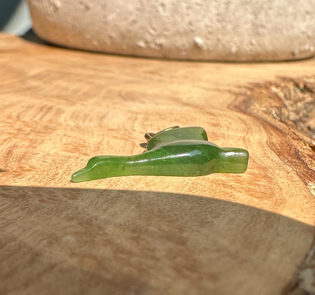 Green jade goose charm with a gold ring bail resting on a wood grain surface