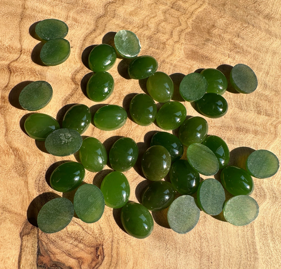 Green Canadian Jade oval cabochons scattered on a wooden surface
