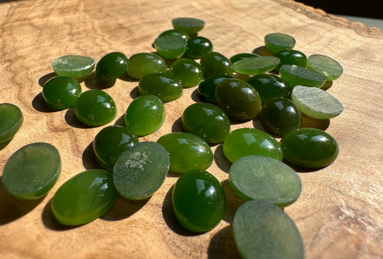 Green oval jade cabochons on wood with polished domed fronts and rough backs