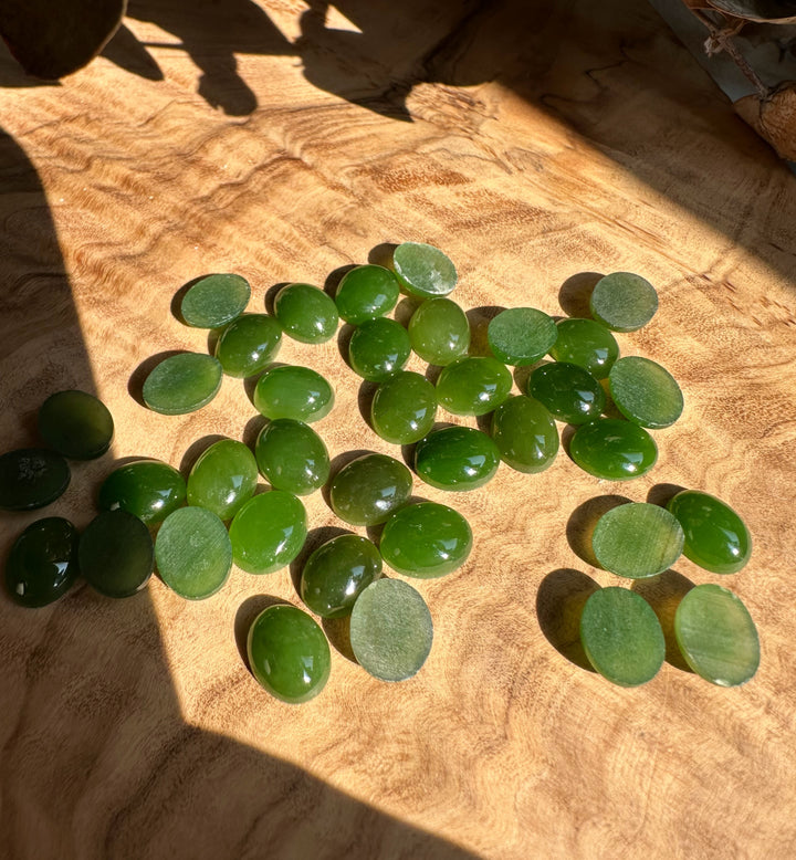 Sunlit group of green oval jade cabochons on wood with backs showing