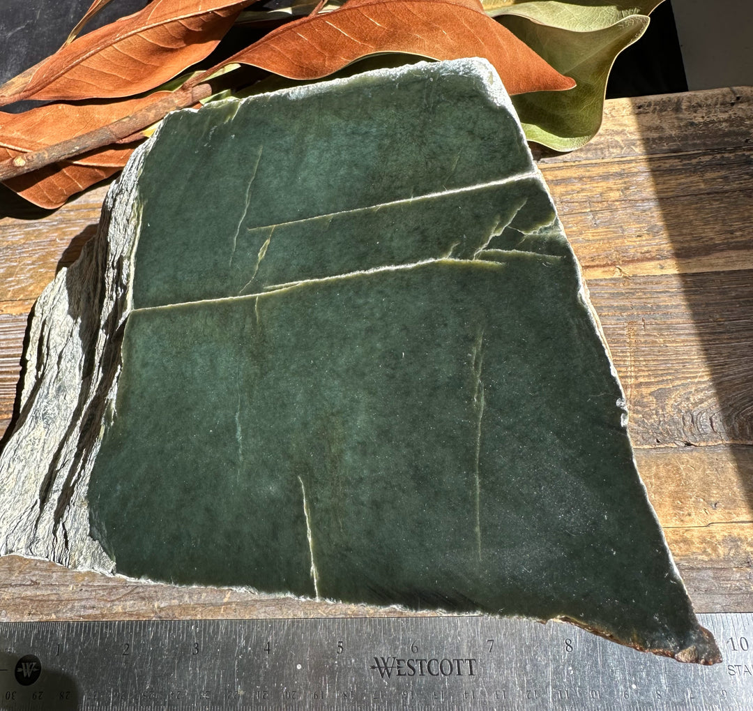 Dark green Wyoming Jade slab with natural fractures and a rough rock edge on a wooden surface.