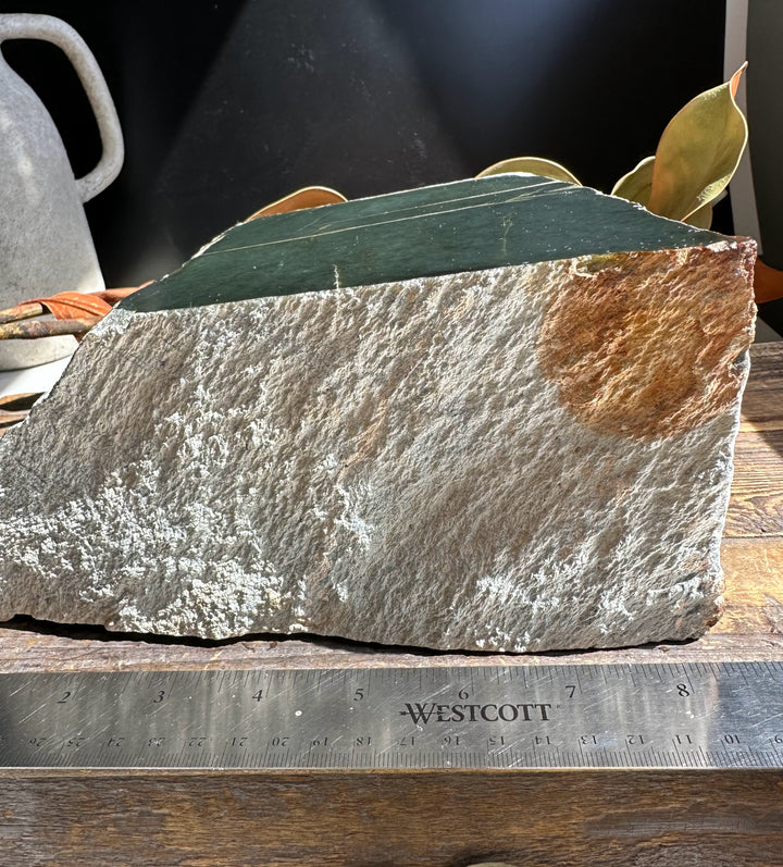 Rough gray host rock with a dark green Wyoming Jade slab on top beside a metal ruler for scale.
