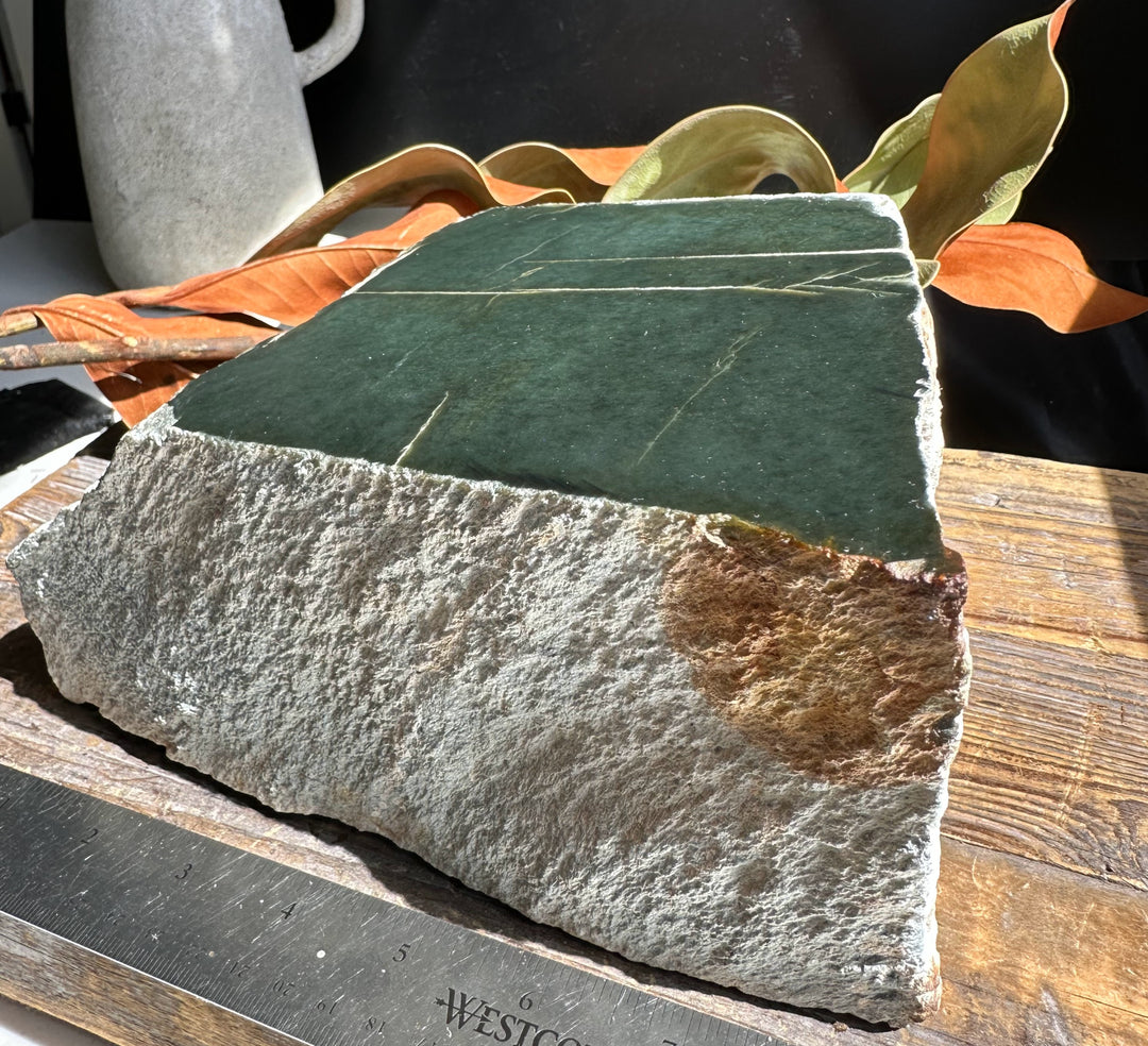 Wyoming Jade block 15.4 lb dark green top resting on rough gray rock with a rust patch and ruler for scale