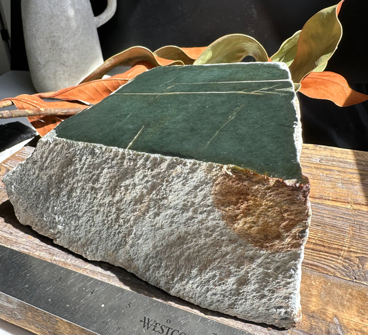 Wyoming Jade block 15.4 lb dark green top resting on rough gray rock with a rust patch and ruler for scale